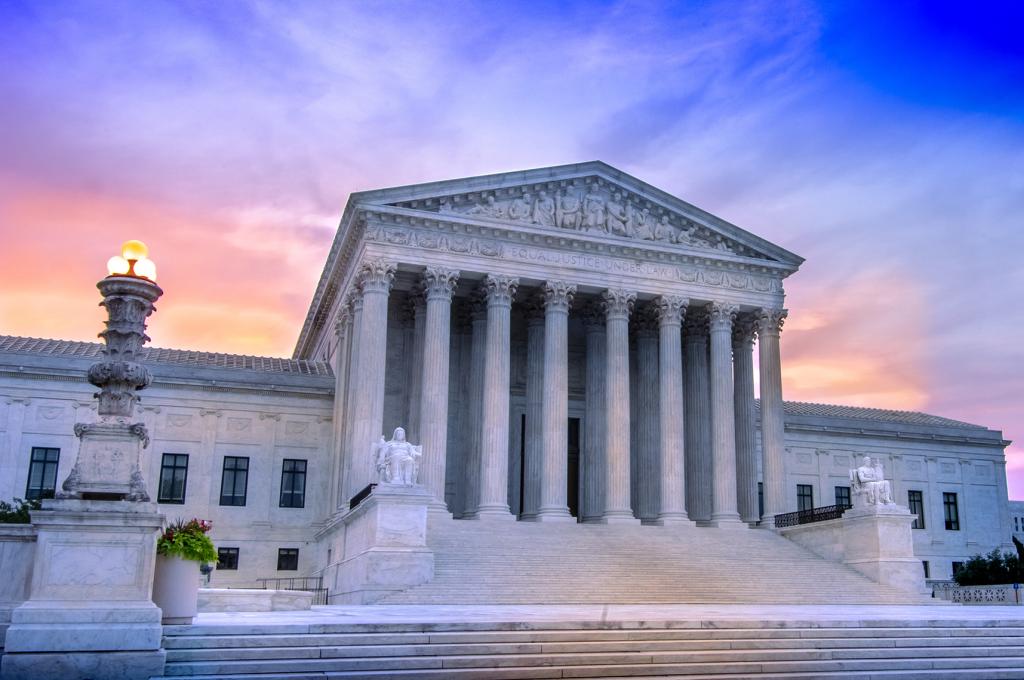 View of marble columns and greek classical architecture of the United States Supreme Court building with sunrise in background.